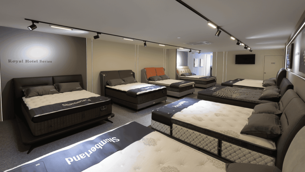 A modern mattress store showroom featuring multiple beds from Slumberland, each displayed with plush headboards and premium mattresses. The space is well-lit with ceiling spotlights and minimalist decor, creating a professional and comfortable shopping environment.